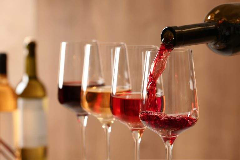 Pouring Wine From Bottle Into Glass On Blurred Background, Close